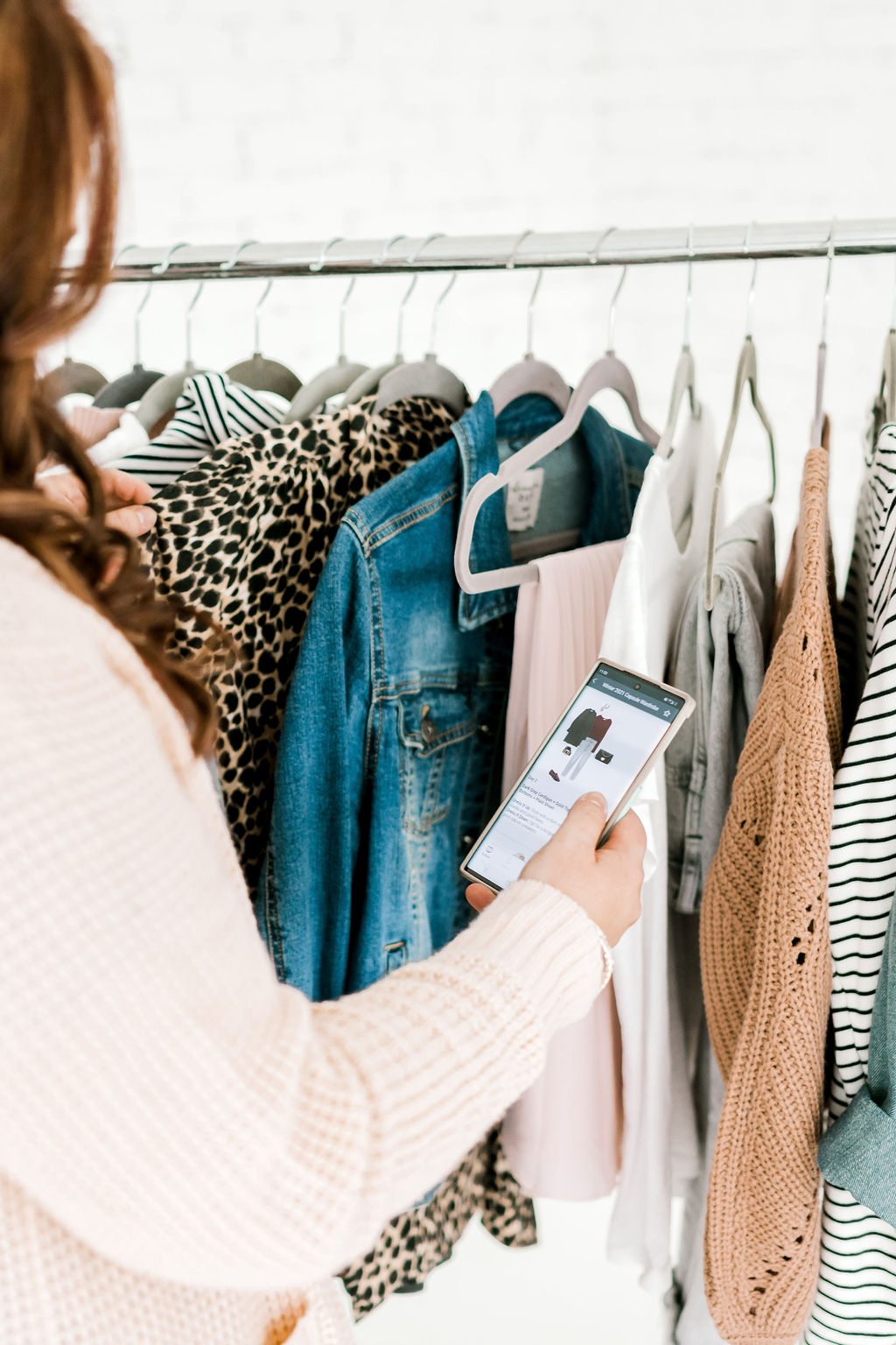 Woman looking at clothes on a rack and comparing to an outfit on her mobile device