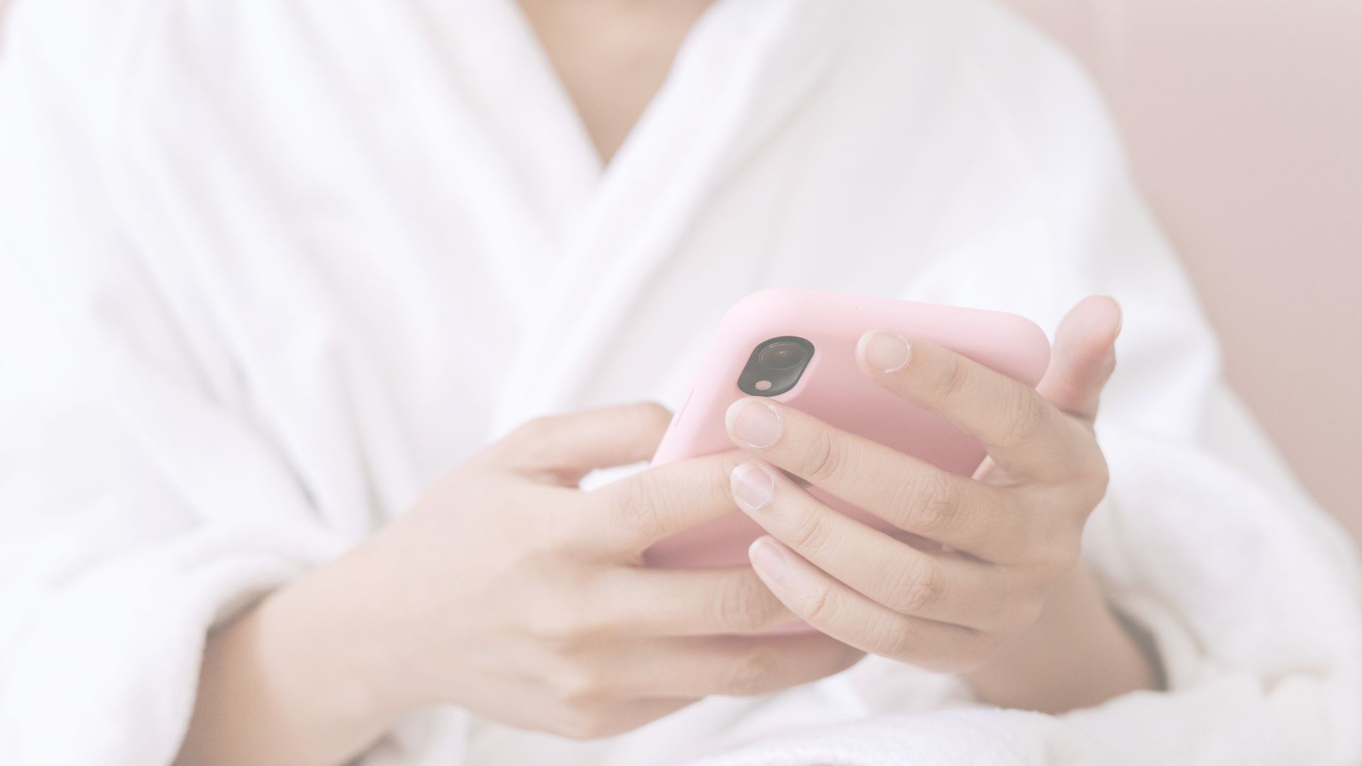 A woman wearing a robe holding a phone in a pink case.